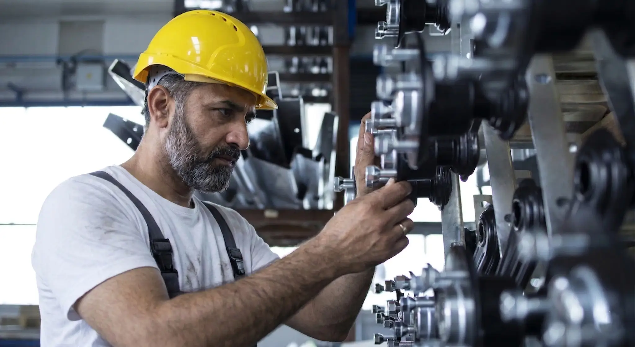 Industrial machine maintenance technician wearing safety helmet inspecting mechanical equipment in factory workshop